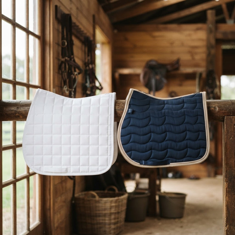 Dressage and jumping saddle pads compared side by side in a tack room