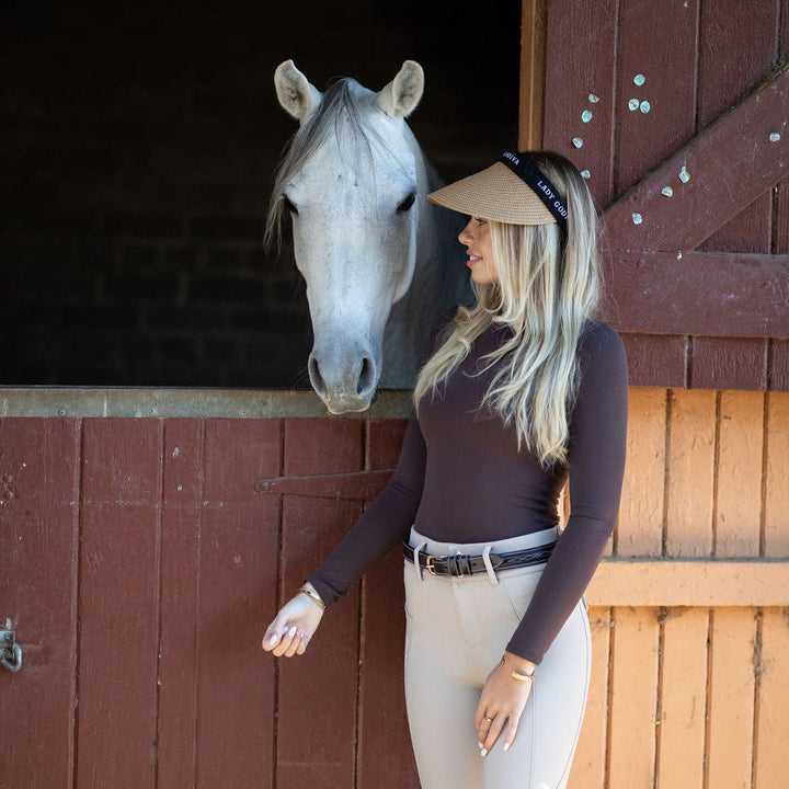 Woman in equestrian attire standing next to a horse in a stable.