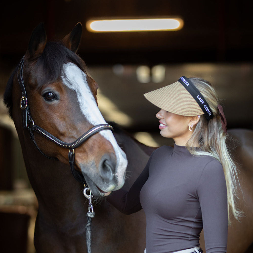 Woman in equestrian attire standing next to a horse indoors.