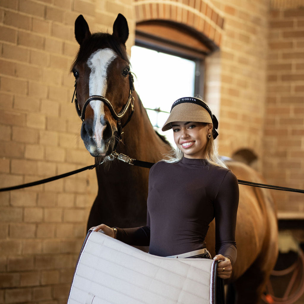 Woman holding a saddle pad next to a horse in an indoor setting
