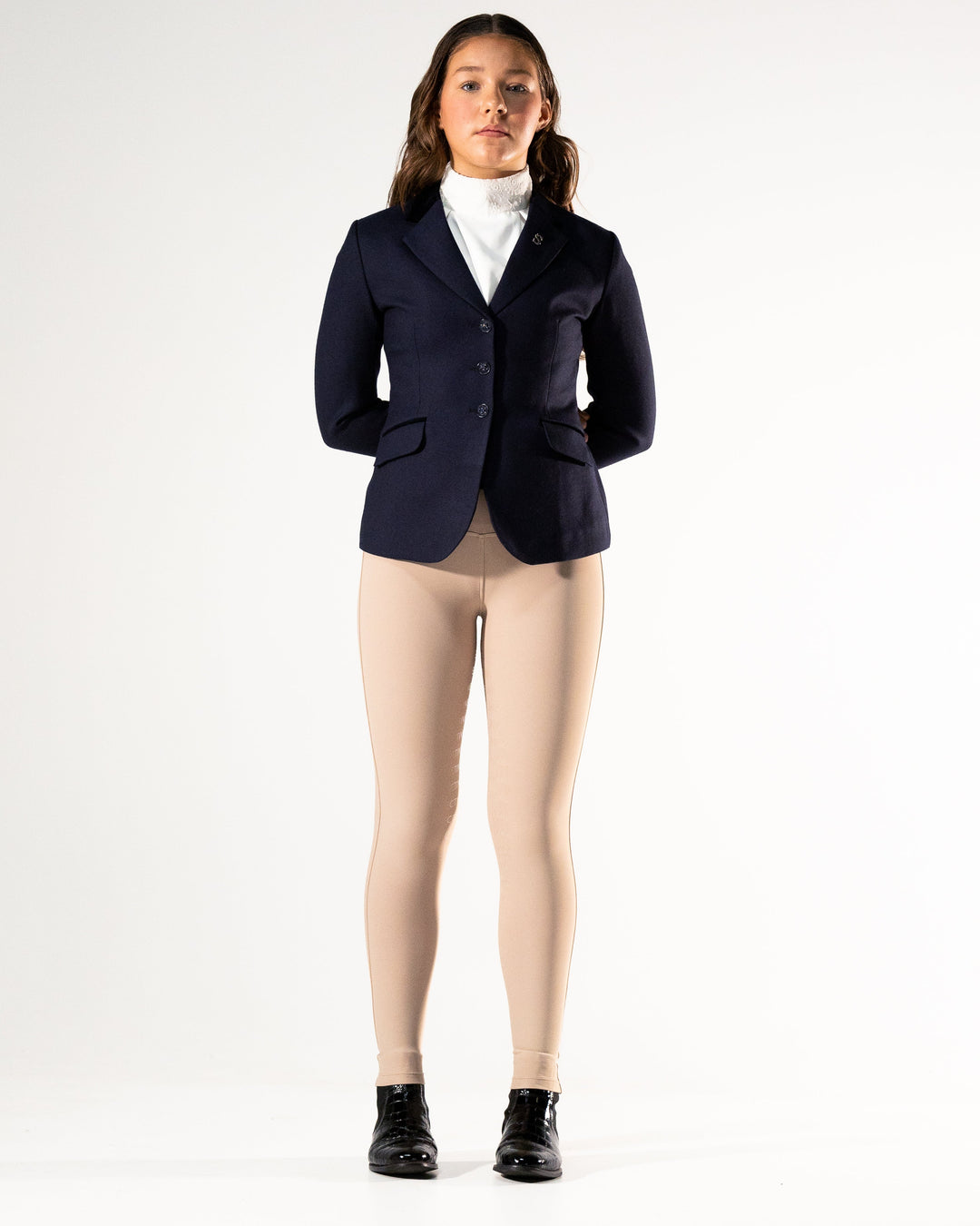 Person wearing a navy blazer, white shirt, beige leggings, and black boots on a white background