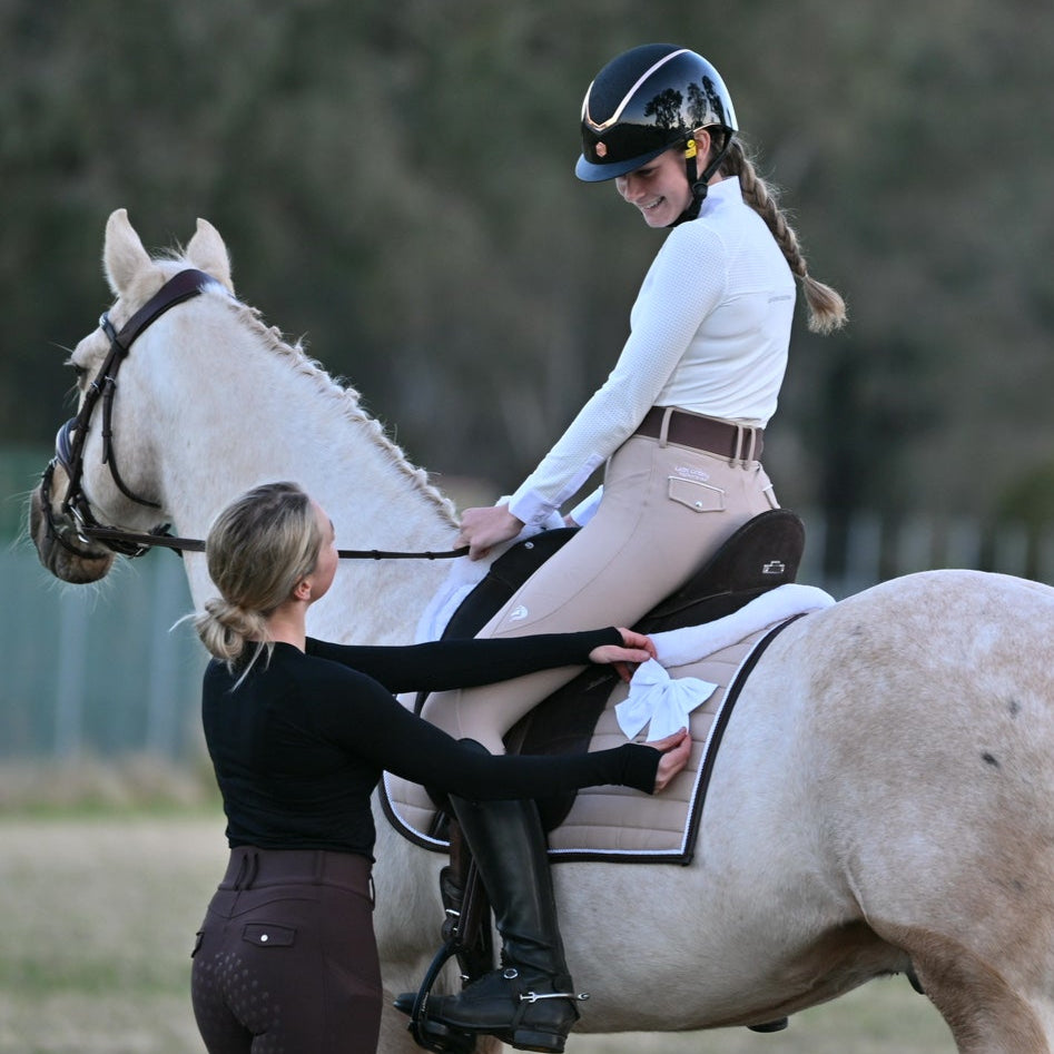Person riding a white horse with another person assisting in an outdoor setting