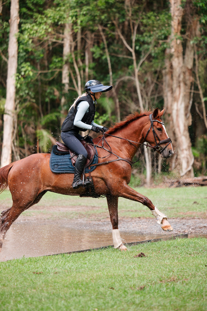 Person riding a brown horse on a path with trees in the background