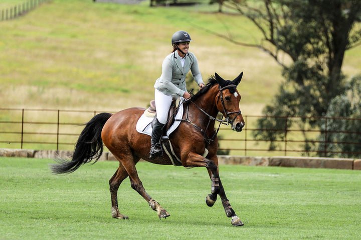 Rider cantering on course wearing Wilma Sport Aero Competition Jacket in Platinum during competition.