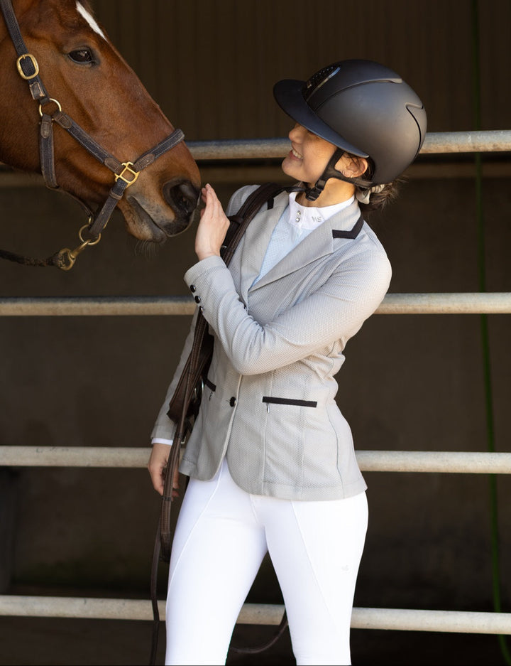 Model wearing Wilma Sport Aero Competition Jacket in Platinum, standing with horse and holding bridle.