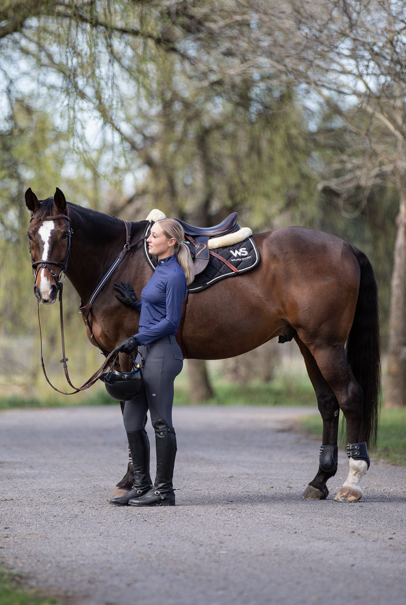 Model with horse, dressed in Featherlight Training Shirt in Urban Navy and Classic Hybrid Breeches in Slate Grey by Wilma Sport.