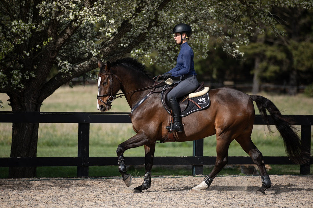 Model riding in Wilma Sport Slate Grey Hybrid Breeches – silicone knee grip breeches and Featherlight Training Shirt in Urban Navy.