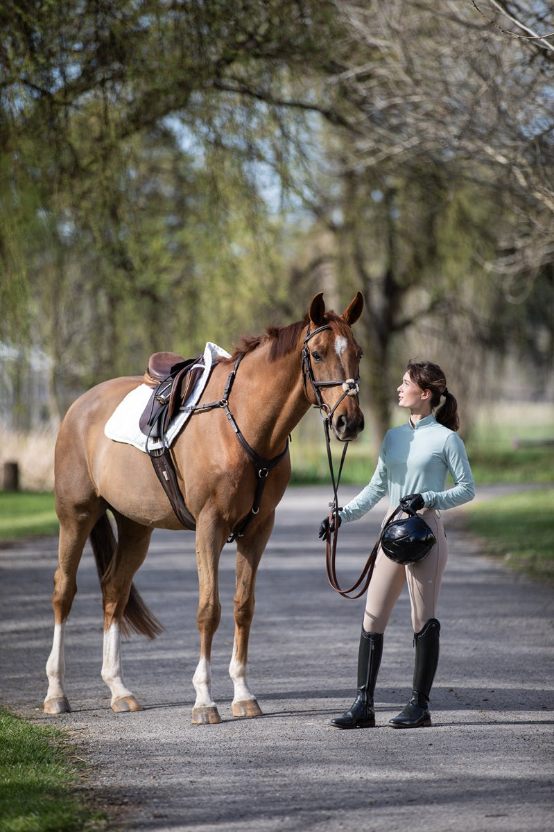 Model wearing Wilma Sport Featherlight Training Shirt in Seafoam with Urban Sand Classic Hybrid Breeches, holding horse outdoors — lightweight UPF30 sun-safe equestrian top.